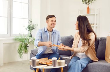 Family Young çifti evdeki kanepede otururken pizza yiyorlar. Lezzetli yemek ya da yemek servisi. Beraberlik ve keyif, öğle yemeğini paylaşmanın basit keyfine dikkat çekmek..