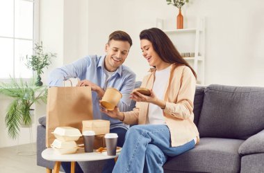 Genç ve mutlu bir çift evdeki oturma odasındaki kutularda yemek yiyip sohbet ediyorlar. Birlikte yemek yiyorlar. Aile yanında hazır yiyecek ve içeceklerle oturuyor. Teslimat hizmeti kavramı.