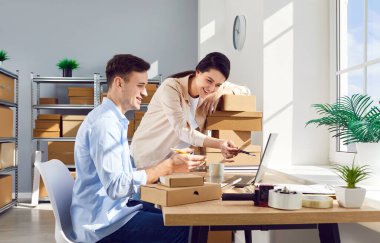 İş arkadaşları paketlerle ve paket kutularıyla çevrili bir dizüstü bilgisayar kullanarak çevrimiçi bir mağazanın deposunda envanter işletiyorlar. Depolama alanında izleme ve düzenleme.