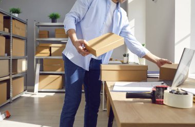 Çevrimiçi bir mağazanın deposunda çalışan bir işadamının orta bölüm çekimi, envanter sayımı, siparişleri işleme koyma ve karton kutu tutma. Depoda işlem yapılıyor.