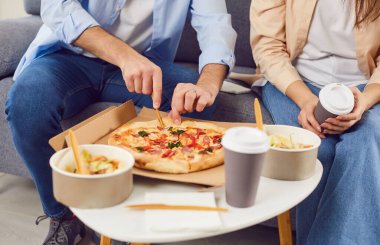 Teslimat ya da paket yemek. Evde pizza, salata ve sıcak kahveyle yemek yiyen genç bir çift. Kanepede oturan ve teslimat servisinden yemek siparişi veren bir çiftin görüntüsü..