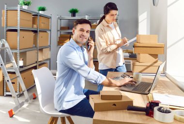 E ticaret deposunda çalışıyorum. Malzeme deposundaki masada oturan erkek yönetici müşteriyi arar, dizüstü bilgisayar kullanır, kadın konsültasyon kontrol listesi göndermeden önce iletişim bilgilerini kontrol eder