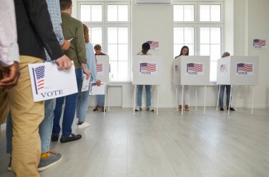 Bir grup farklı Amerikan vatandaşı seçim günü oy kullanma merkezinde kayıt yaptırıyor ve oy pusulalarını oy verme kabinine koyuyorlar. ABD 'li seçmenler oy merkezinde kuyrukta bekliyorlar.