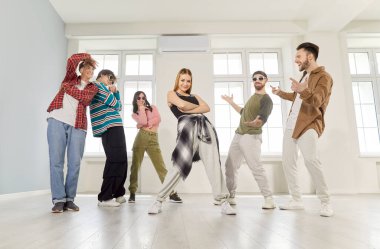 Dans eden havalı gençlerden oluşan bir grup aktif olarak içeride dans ediyor, hareketli ve poz veriyor modern stüdyo ortamında, etkileşimde, lider kadın özgüvenle dans ediyor, dans ediyor veya dans ediyor. 