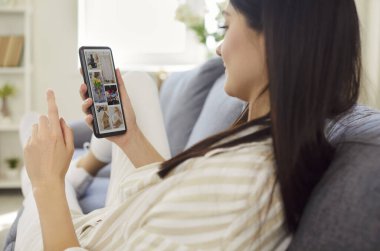 Evde cep telefonu kullanan bir kadın, ekranda metin okuyor, resim izliyor, pazar fotoğrafı izliyor, internette sohbet ediyor, iyi haberler alıyor, online uygulama üzerinden sipariş veriyor, alışveriş yapıyor, işbirliği yapıyor, takım sohbeti yapıyor.