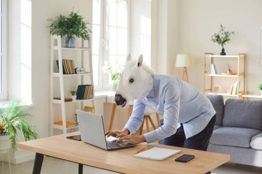 Eşek giyen komik, mutlu adam, at kafası online tabletle çalışıyor, klavyede yazıyor, e-posta ya da mesaj yazıyor, sohbet ediyor, alışveriş yapıyor, yakışıklı adam modern oturma odasında oynuyor.