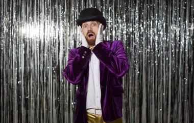 Mor kostümlü korkmuş ve korkmuş bir adamın portresi. Parlak bir arka planda, bir partide. Anlamlı korku ve korku dolu tepkiler kutlamanın dramatik atmosferini daha da artırıyor..