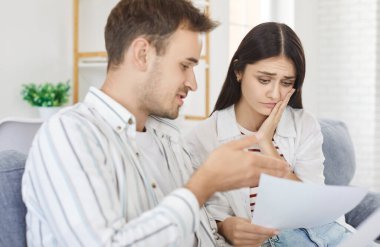 Üzgün genç bir çift kanepede oturuyor ve evdeki mali belgelere bakıyorlar. Hayal kırıklığına uğramış erkek ve kadın faturaları kontrol ediyor, gelir ve kar planlama aile bütçesini sayıyor.