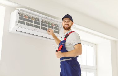 Evdeki klimayı inceleyen mutlu bir teknisyenin ya da işçinin portresi. Profesyonel adanmışlık ve hizmet, konut ortamında onarım çalışmalarının memnuniyetini yakalamak..