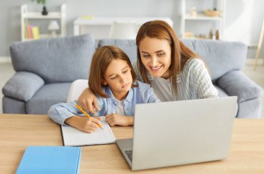 Anne ve küçük okul öğrencileri evde öğreniyor, küçük çocuk derslerle meşgul, akıllı çocuk bilgisayar başında uzaktan çalışıyor, deftere yazı yazıyor, öğretmenlik yapıyor. 