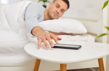 Adam sabah erken saatlerde mobil alarma ya da telefona uyanır. Yataktaki uykulu adam elini uzatıp aramayı geri çevirir ya da çalar saatin uykusuna basar. Yakın plan bulanık arkaplandaki telefonu alır