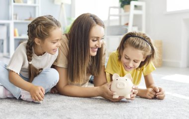 Mutlu aile, çocuklar ve anne birlikte para biriktiriyorlar, domuz kumbarasıyla oynuyorlar, ebeveynler, çocuklar evde, küçük oğlu ve kızına yatırım yapmayı öğretiyorlar para planlama hayatı, finansal gelecek, tasarruf hesapları.