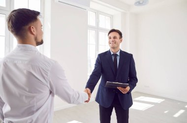 Profesyonel emlakçı temsilcisi, imzalı kontratıyla boş dairelerde duruyor ve mutlu müşteri ve yeni ev sahibiyle anlaşma yapıyor. Emlak piyasası kavramı.