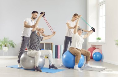 Klinikte rehabilitasyon sırasında, fizyoterapistlerin yardımıyla esneme egzersizleri yapan yaşlı çift. Yaşlı hastalara rehberlik eden ve onları destekleyen iki doktor, hareket ve refahları üzerinde çalışıyorlar..