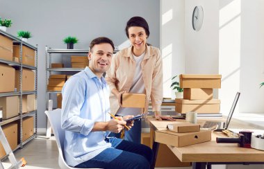 Genç mutlu iş arkadaşları iş yerindeki depodaki kameralara bakıp stok ve envanteri kontrol ediyorlar. Şirket çalışanları karton kutularla dolu perakende deposunda sipariş hazırlıyorlar..