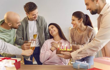 Gülümseyen genç insanlar ellerinde şampanya kadehleriyle mutlu kız arkadaşlarını tebrik ediyorlar doğum gününde masada oturuyorlar ve ona evde pasta veriyorlar. Doğum günü partisi ve kutlama konsepti.