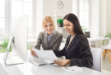 Meslektaşlar ofis toplantısı sırasında belge ve bilgisayarla birlikte çalışır, profesyonel bir ortamda iş birliği ve hassasiyet üzerine odaklanırlar..