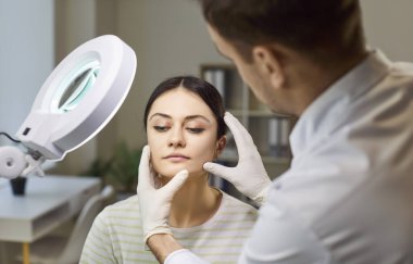 Dermatolog doktor cilde yakından bakıyor. Dermatoskop profesyonel enstrüman, cam lamba, dermatoloji kliniği danışmanı, güzellik tedavisi planlıyor.