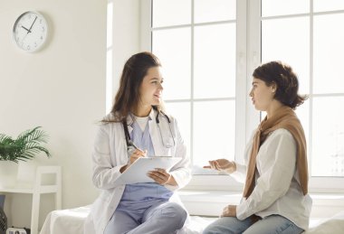 Kanepede oturan genç bir kadın, doktorla sağlık sorunlarını tartışıyor. Konsültasyon sırasında dinleyen ve not alan kadın doktor veya kardiyolog, hasta şikayetleri üzerine yoğunlaşıyor.