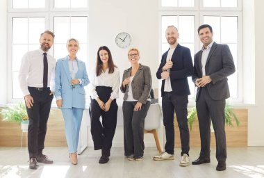 Ofis ortamında bir arada duran altı iş adamının portresi. İş elbiseli erkek ve bayan meslektaşlar sıraya dizilip gülümserken güven yayıyorlar.