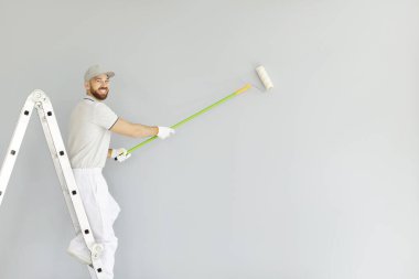 Tadilat sırasında duvarları boyarken elinde fırça tutan gülümseyen bir ressamın portresi. İnşaat, onarım ve dekoratif gelişmelere profesyonel yaklaşımın vurgulanması.