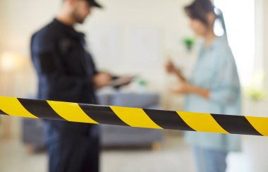 Genç erkek polis eve girdikten sonra kadın kurbanla görüşüyor. Polis memuru, kadını sorgulayan ifadeleri panoya yazıyor. Suç, soygun, mülkiyet güvenliği kavramı.