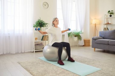 Denge için stabil top egzersizi, halter, fitness, yaşlı sporcu kadın, evde yalnız başına huzur dolu eski yoga, stres atma, enerji tazeleme, yaşlılar sağlıklı yaşam tarzını takip eden fiziksel egzersizler yapıyor.