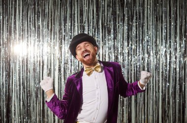 Parlak mor takım elbiseli, eldivenli ve şapkalı mutlu komik adamın portresi parlak gümüş folyo arka planda eğleniyor. Disko partisinde dans eden heyecanlı bir şovmen. Kutlama konsepti.