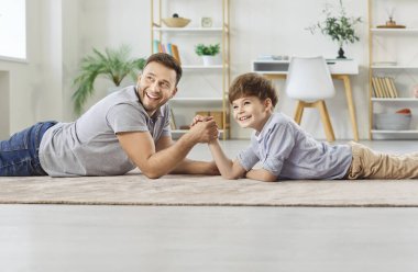 Baba ve oğul, baba küçük tatlı oğluyla oynamaktan mutlu evde bilek güreşi yapmaktan, neşeli, sevgi dolu ebeveyn eğlencesi savaş sporlarıyla meşgul olmaktan, hafta sonlarını birlikte geçirmekten mutlu. 