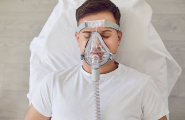 Hastane yatağında oksijen maskesi takmış beyaz bir adamın portresi. Havalandırma, solunum cihazları olan hasta hasta acil solunum desteği için. Yakın çekim, üst görüntü.