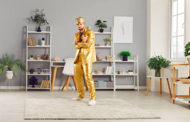 Evdeki oturma odasında elinde altın külçeyle duran kendinden emin, komik bir gencin uzun portresi. Altın takım elbiseli ve şapkalı zengin adam içerde kameraya neşeli görünüyor. İş başarısı konsepti.