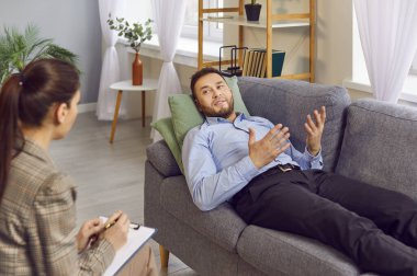 Terapi seansı sırasında erkek hasta psikoterapistle konuşuyor. Yetişkin bir adam kanepede uzanıyor, düşüncelerini kadın terapistle paylaşıyor ve tavsiye istiyor. Psikoterapi kavramı