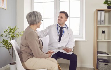 Tıbbi klinikteki kıdemli hasta, steteskop takan ve muayene sırasında randevusuyla birlikte rapor tutan erkek arkadaş canlısı doktorla konuşuyor. Doktor destek konsepti.