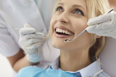 Gülümseyen kadın hasta klinikteki dişçi randevusuna gidiyor, doktor diş ve ağız bakımını kontrol ediyor, profesyonel bir ortamda dişçilik hizmetine odaklanıyor..