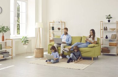 Aile, evinde kablosuz internet bağlantısı olan rahat İskandinav oturma odasında oturuyor, çocuklar dizüstü bilgisayarda ve tablette video izliyor, ebeveynler kendi cihazlarını kullanıyor. İnsanlar, teknoloji kavramı