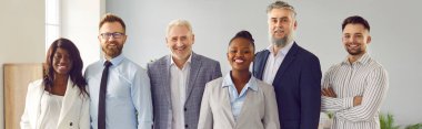 Çok ırklı iş adamları, kameraya bakıp içeride gülümseyen kadın ve erkekler. Şirket çalışanları ya da bir grup personel güvenle ofiste duruyorlar. Takım çalışması konsepti. Pankart.
