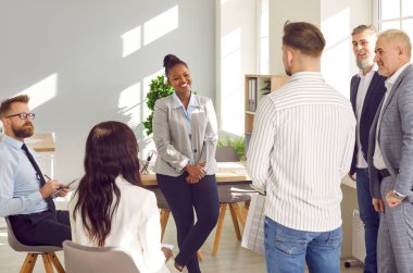 Ofisteki toplantı odasında iletişim kuran gülümseyen çeşitli meslektaşlar. Kendine güvenen, çok ırklı ofis çalışanları gündelik kıyafet hakkında konuşuyor, personel toplantısında mali istatistikleri tartışıyorlar.