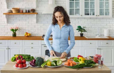 Neşeli genç bir kadının portresi mutfakta duran bir sürü sebzeli taze sağlıklı vegan salatası hazırlıyor. Evde yemek yapan bir kadın. Vejetaryen yiyecekler, diyet ve beslenme konsepti.