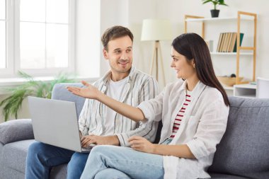 Modern oturma odasındaki koltukta oturan, dizüstü bilgisayara bakan, internetten bilet alan, e-ticaret perakende e-hizmetleri kullanan, rahat hayatın tadını çıkaran, planlayan ve tartışan çekici bir çift. 