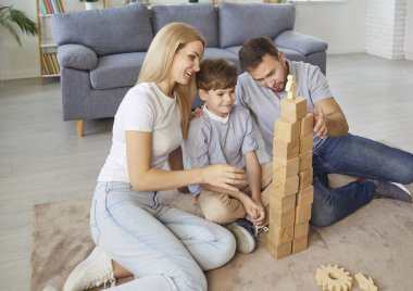 Mutlu ebeveynler oğluyla vakit geçirir, tahta küplerle eğitici oyunlar oynarlar. Anne, baba ve çocuk blokları istiflemek, inşaatın tepesinde oyuncak insan olan yapı kulesi.