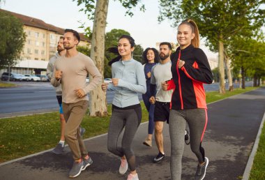 Bir grup enerjik arkadaş güzel bir parkta koşuyor, fitness ve takım çalışmasını destekliyorlar. Bir grup insan sabah bir şehir caddesinde koşuyor..