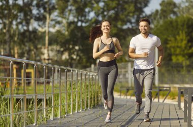 Sportif dost canlısı insanlar aktif olarak dışarı koşuyor, sağlıklı görünüşlü çiftler sağlıklı koşulardan keyif alıyorlar, yaz günü spor kıyafetleri, pantolonlar giyerek spor yapıyorlar, yürüyüş yolunda ilerliyorlar. 