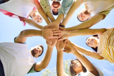 Genç mutlu insanların ya da bir grup öğrencinin alt görüşü açık havada toplanıp kollarını mavi gökyüzü arka planında bir yığın haline getirmek. Arkadaşlık, birlik ve takım çalışması kavramı.