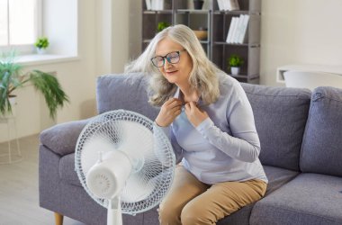 Son sınıf öğrencisi kadın, elektrikli vantilatörün serin havasının keyfini çıkarıyor, oturma odasının içindeki koltukta oturuyor. Sıcak yaz ve hava yüzünden aşırı ısınmış yaşlı bir bayan. Isı, yaşam tarzı konsepti