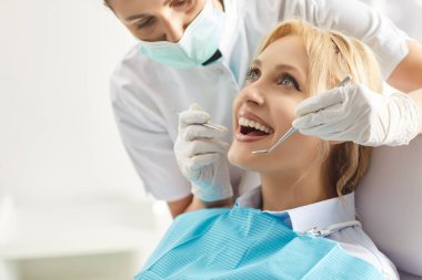 Kadın hastaların dişlerini tedavi etmek için dişçi aletleri kullanan profesyonel bir stomatolog. Modern diş sağlığı kliniğine giden, düzenli check-up yaptıran diş beyazlatma tedavisi gören bir kadın.