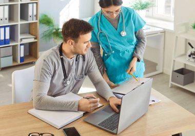 Erkek doktor ve kadın hemşire evrak işlerinde yardım ediyor, hasta testlerinin sonuçlarını tartışıyor, plan tedavisini tartışıyorlar. Profesyonel ortamda işbirliği. Sağlık personeli