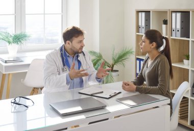 Muayene sırasında klinikteki masada oturan dost canlısı erkek doktorun tavsiyelerini dinleyen genç bir hastanın portresi. Sağlık ve Tıp Konsepti.