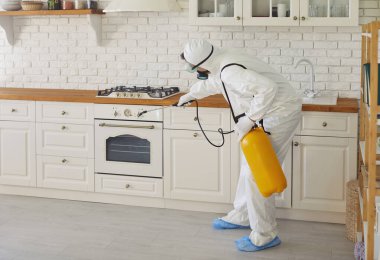 Beyaz üniformalı ve koruyucu maskeli bir adam mutfağı temiz tutmak için böcek ilacı püskürtüyor. Haşere Kontrol Servisi dezenfekte servisinden bir uzman. Güvenli ortam