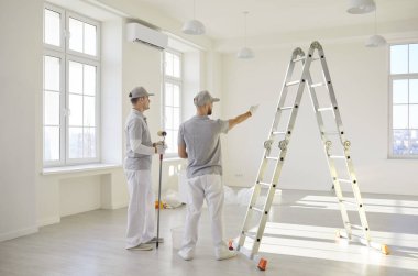 İki profesyonel müteahhit işçi üniformalarıyla boş bir odada merdivenin başında, yenileme işlerini tartışıyorlar. Erkek ressamların yeni apartmanda tasarım projesi hakkında konuştuklarının arka planı.