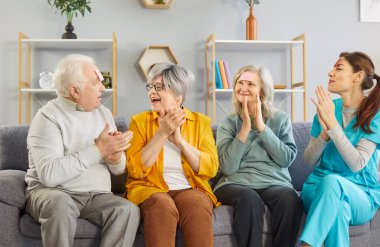Huzurevinden son sınıflar ve bakıcıları birlikte eğleniyor ve oyun oynuyorlar. Ben kimim ki kanepeye oturmuş, alnımda çıkartmalarla el çırpıyorum, mutlu bir şekilde gülüyorum.